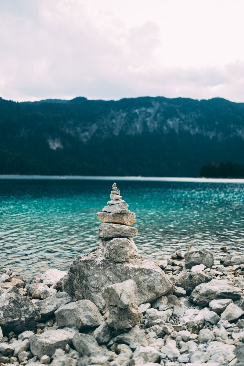 Peaceful lake view with stacked stones against mountain backdrop, ideal for nature themes.